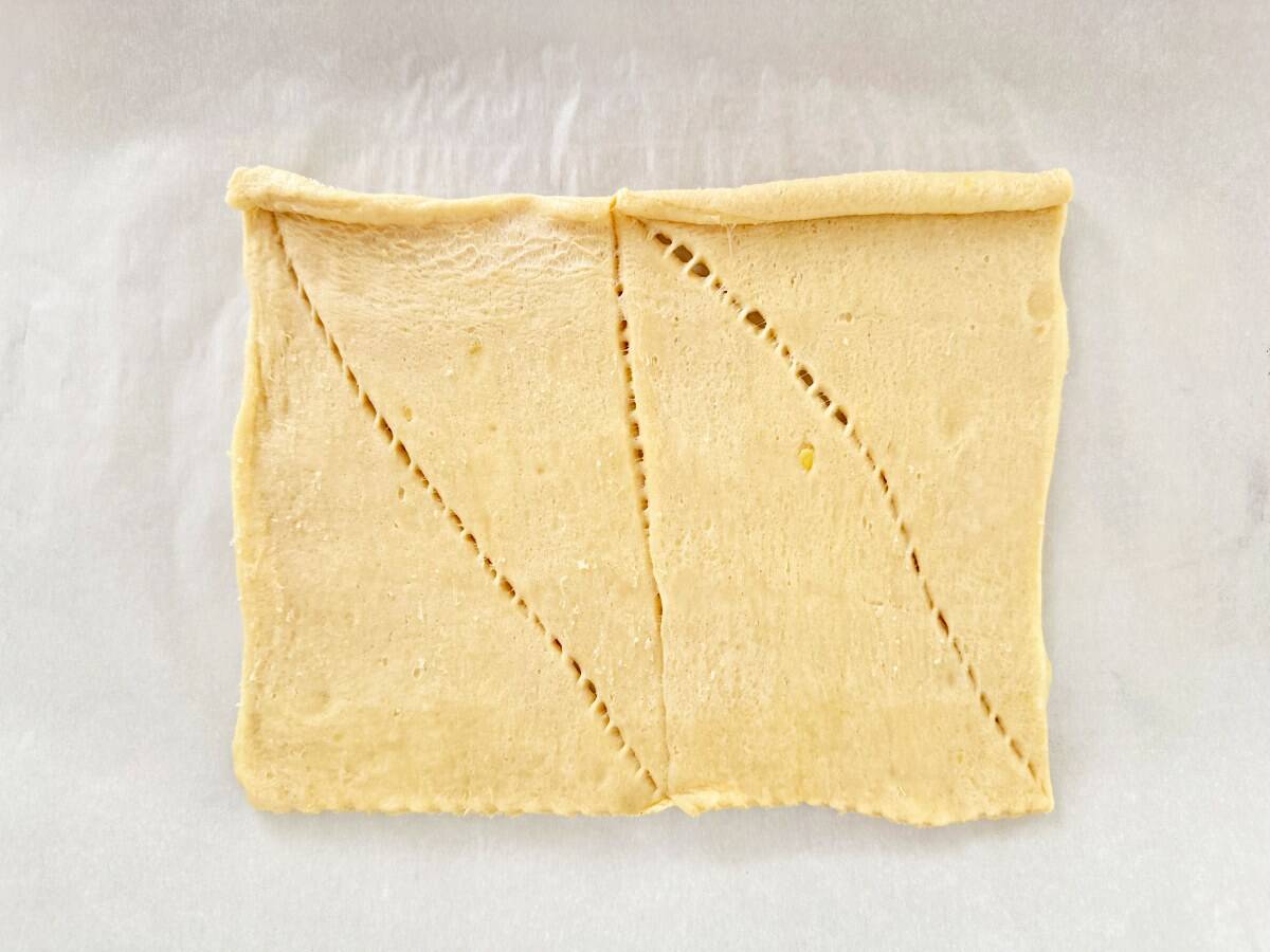 Unrolled crescent dough on white parchment paper.